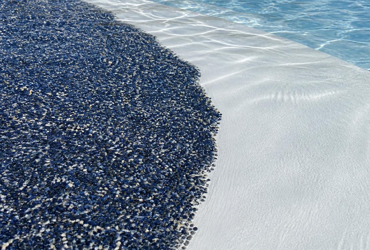 Close-up of a pool interior showing dark blue pebble aggregate finish next to smooth white plaster