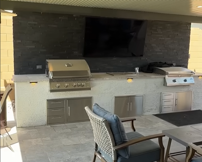 Outdoor kitchen island with built-in grill, refrigerator and stone counter on a covered Arizona patio